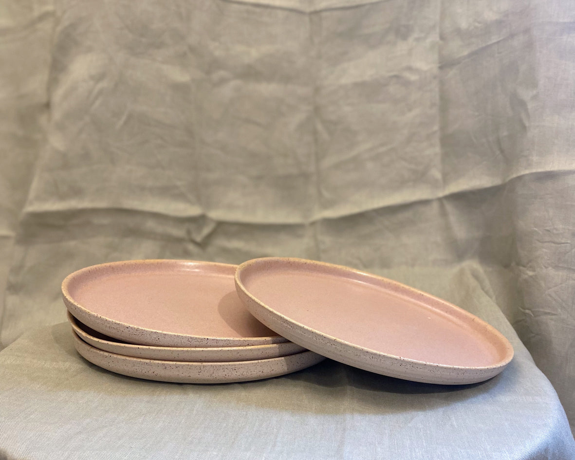 A stack of 4 blush pink plates, with one plate resting on top of the stack.